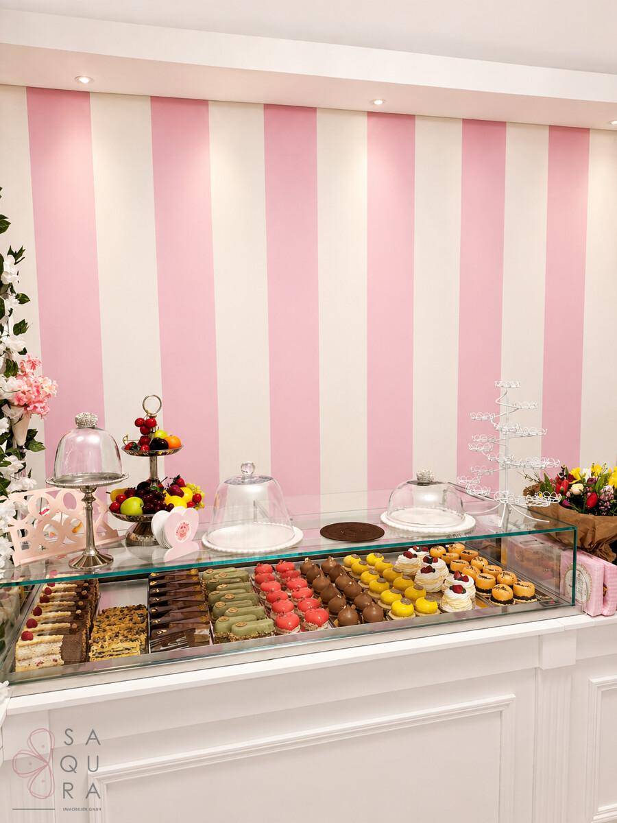 Nahaufnahme einer Glasvitrine mit einer großen Auswahl an bunten Kuchen und Desserts vor gestreiften Wänden.