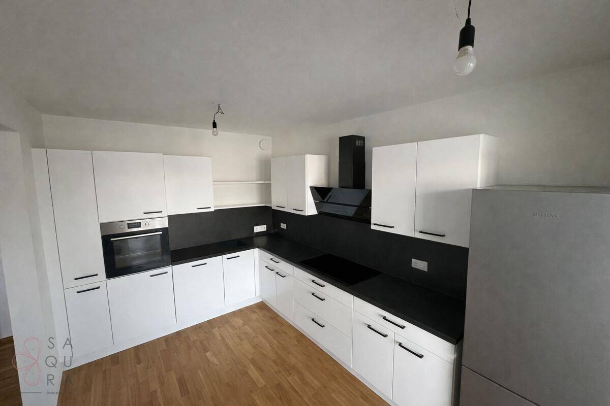 Neue Küche mit weißen Fronten, schwarzer Arbeitsplatte, integriertem Backofen und Holzboden.