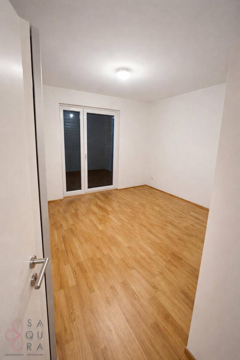 Leeres Schlafzimmer mit Holzboden und großen Fenstertüren, die viel Tageslicht hereinlassen.