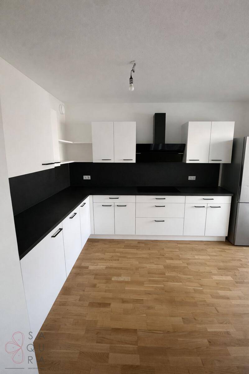 Moderne Küche mit weißen Schränken, schwarzer Arbeitsplatte und Holzboden, bereit für die Installation von Geräten.
