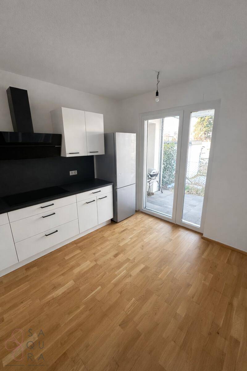 Helle Küche mit weißen Schränken, Holzboden und Zugang zu einem kleinen Außenbereich.