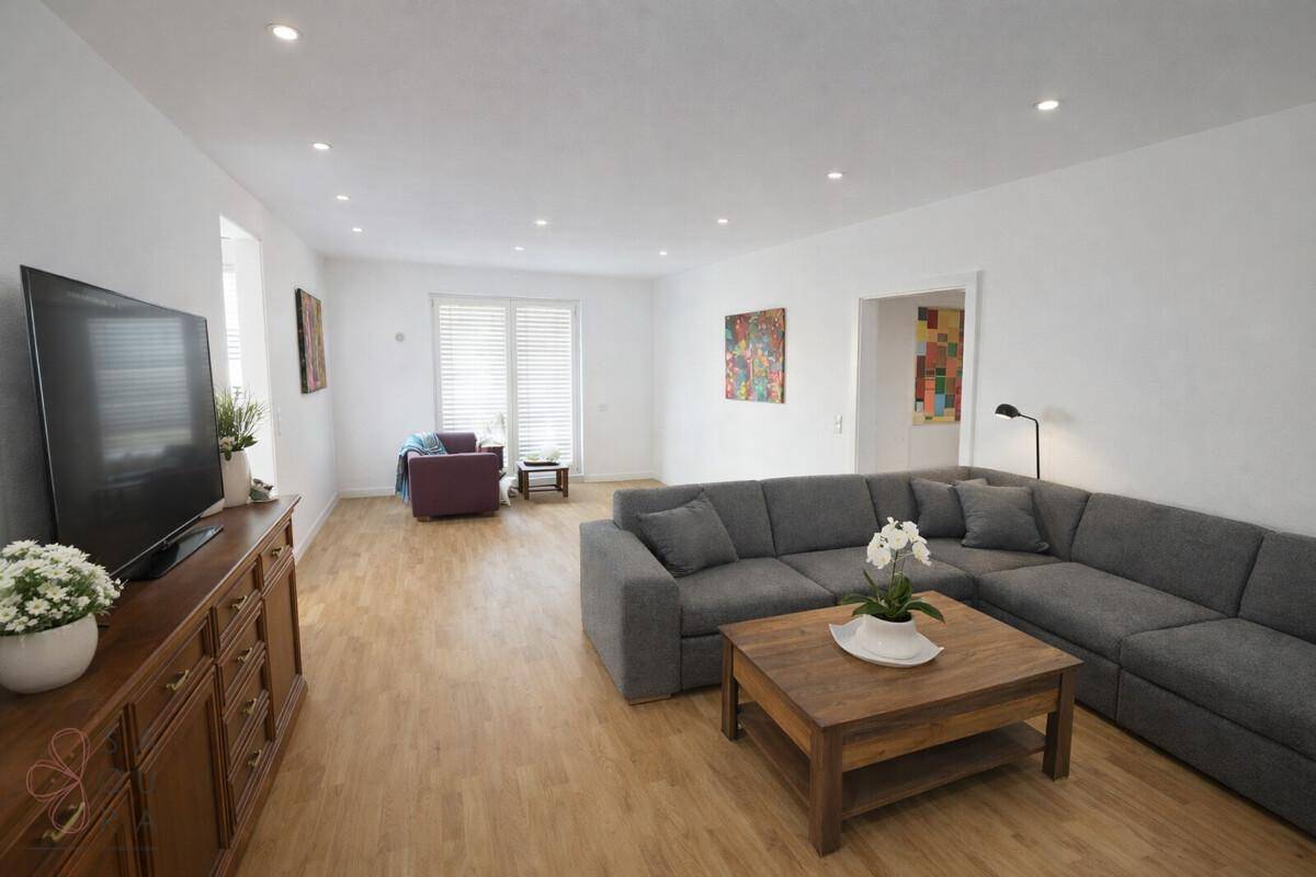 Geräumiges Wohnzimmer mit modernem Ecksofa, Holzboden und integrierten Deckenleuchten.
