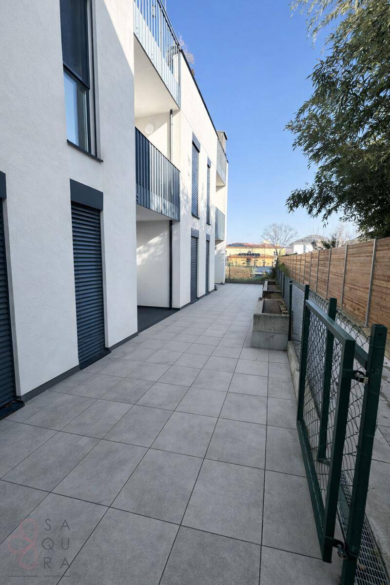 Lange, geflieste Terrasse entlang der Gebäudeseite mit Blick ins Grüne.