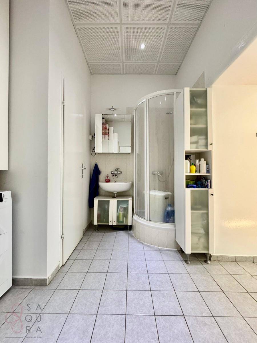 Funktionales Badezimmer mit Eckdusche, Waschbecken und Fliesenboden, inklusive Waschmaschinenanschluss.
