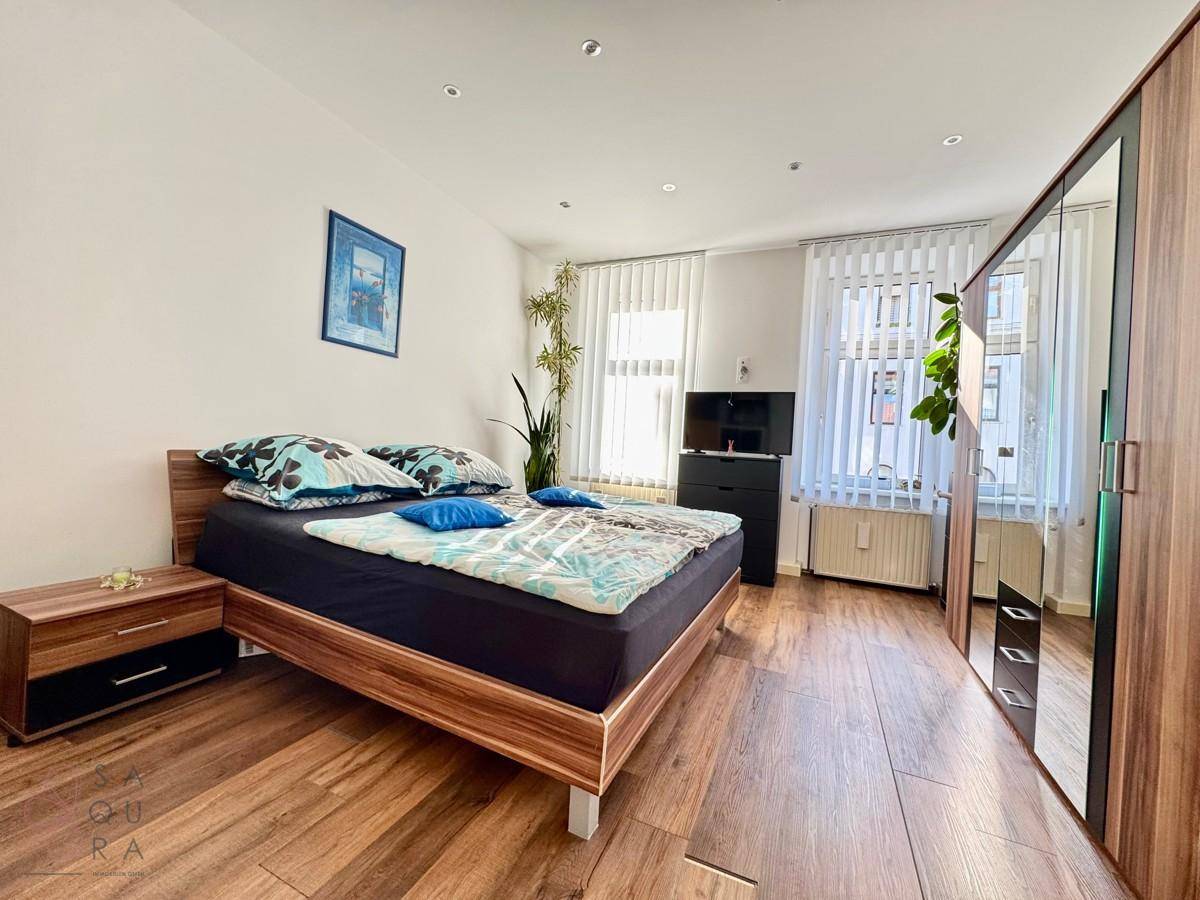 Gemütliches Schlafzimmer mit Holzbett, großem Kleiderschrank und viel Tageslicht durch die Fenster.