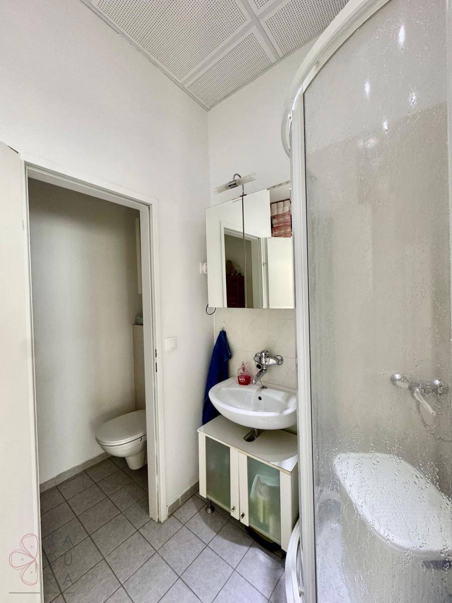 Helles Badezimmer mit praktischer Eckdusche und Waschbecken, angrenzend an eine separate Toilette.