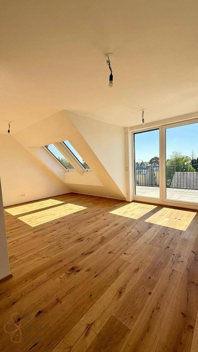 Geräumiges, leeres Zimmer mit Holzboden, großen Fenstern und viel Tageslicht von oben.