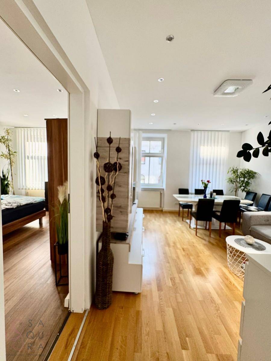 Offener Übergang vom Wohnbereich zum Schlafzimmer mit durchgehendem Holzfußboden und heller Einrichtung.