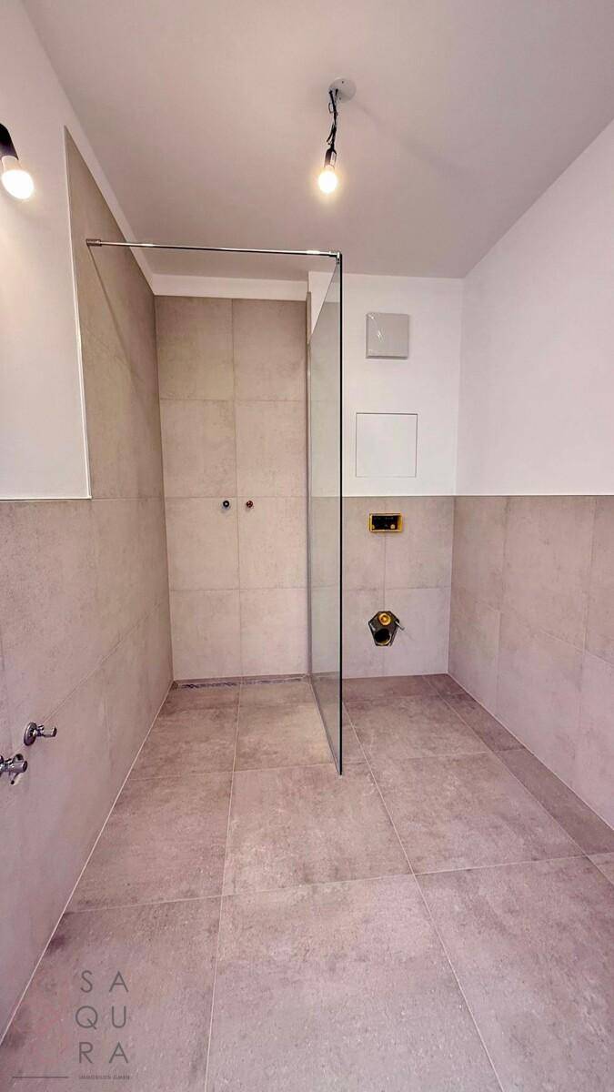 Unmöbliertes Badezimmer mit Fliesenboden, begehbarer Dusche und vorbereiteten Anschlüssen.