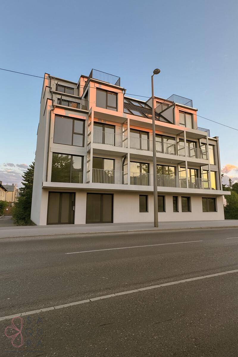 Modernes Mehrfamilienhaus mit klaren Linien, großen Glasflächen und mehreren Balkonen.