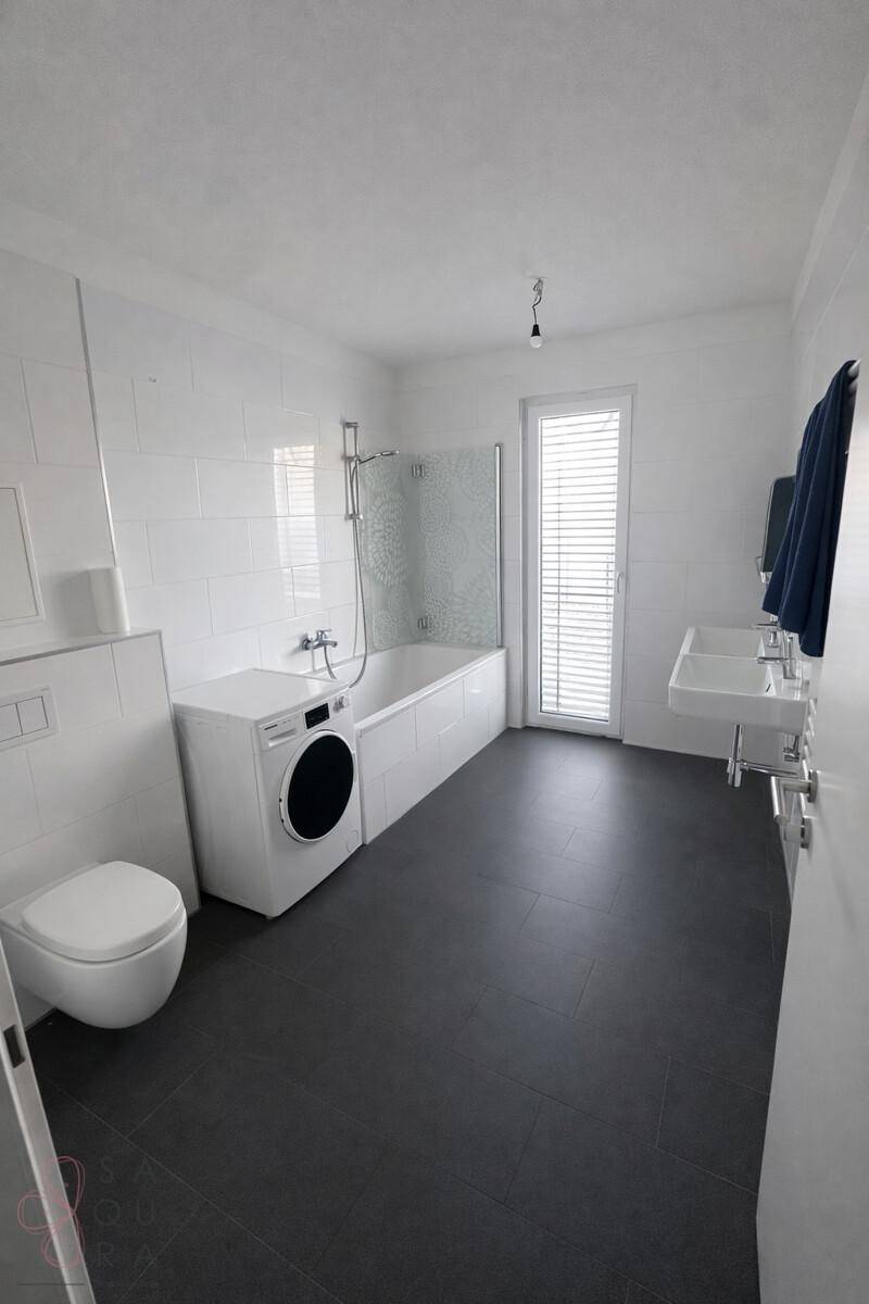 Modernes Badezimmer mit Badewanne, Dusche, Doppelwaschbecken und Waschmaschine.