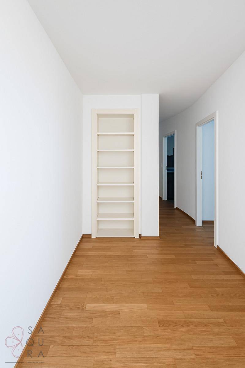 Heller Flur mit Holzboden und praktischem Einbauregal, der zu weiteren Räumen führt.