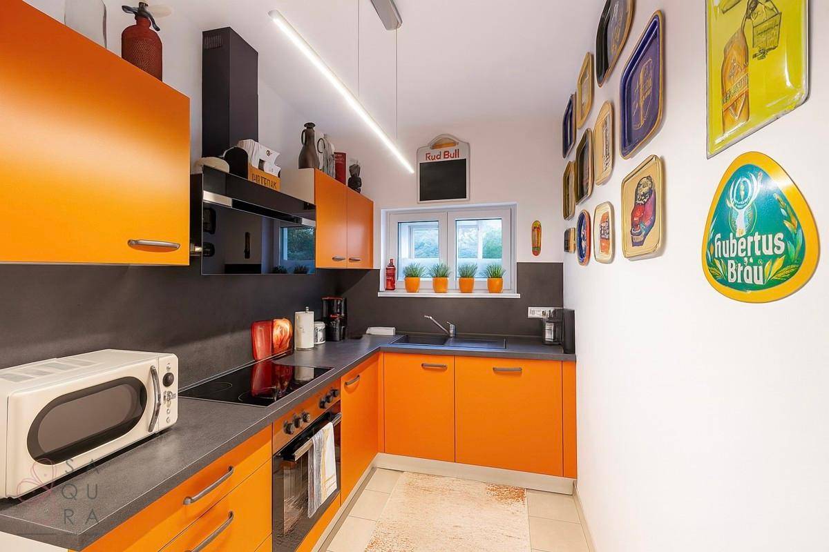 Moderne Küche mit orangefarbenen Schränken, dunkler Arbeitsplatte und Fenster.