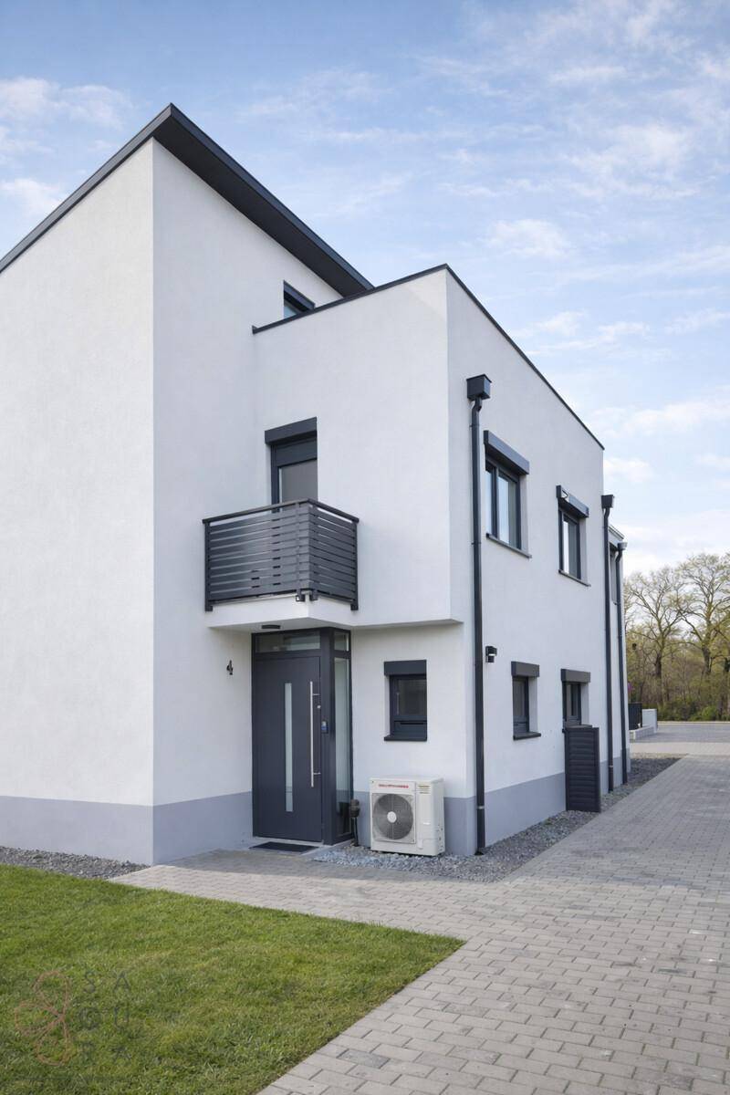 Ansicht des modernen Reihenhauses mit Wärmepumpe und kleinem Balkon am Eingang.