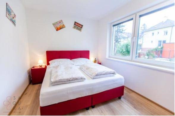 Helles Schlafzimmer mit rotem Bett, Holzboden und großem Fenster.