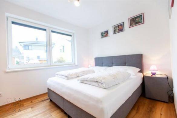 Helles Schlafzimmer mit grauem Bett, Holzboden und Blick ins Grüne.