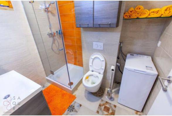 Modernes Badezimmer mit Dusche, WC und Waschmaschine, orangefarbene Akzente.