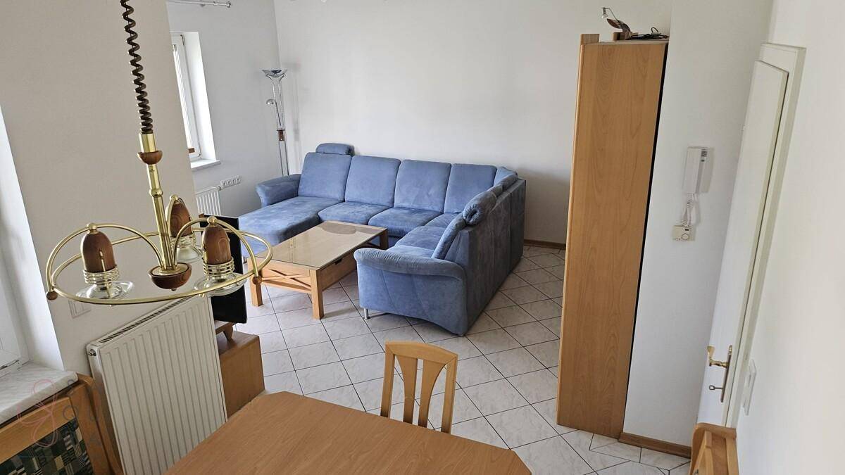 Kombinierter Wohn- und Essbereich mit Fliesenboden, Holztisch und blauer Couch.