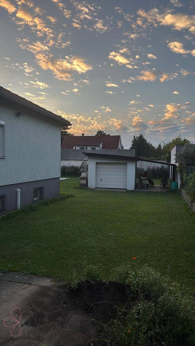 Weitläufiger Gartenbereich mit Garage und Nebengebäuden unter einem bewölkten Abendhimmel.