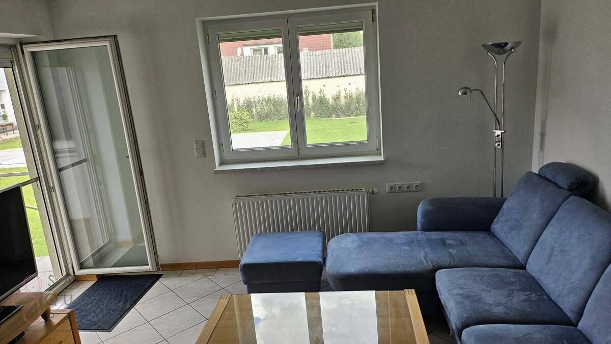 Helles Wohnzimmer mit blauer Eckcouch, Fliesenboden und Zugang zum Garten.