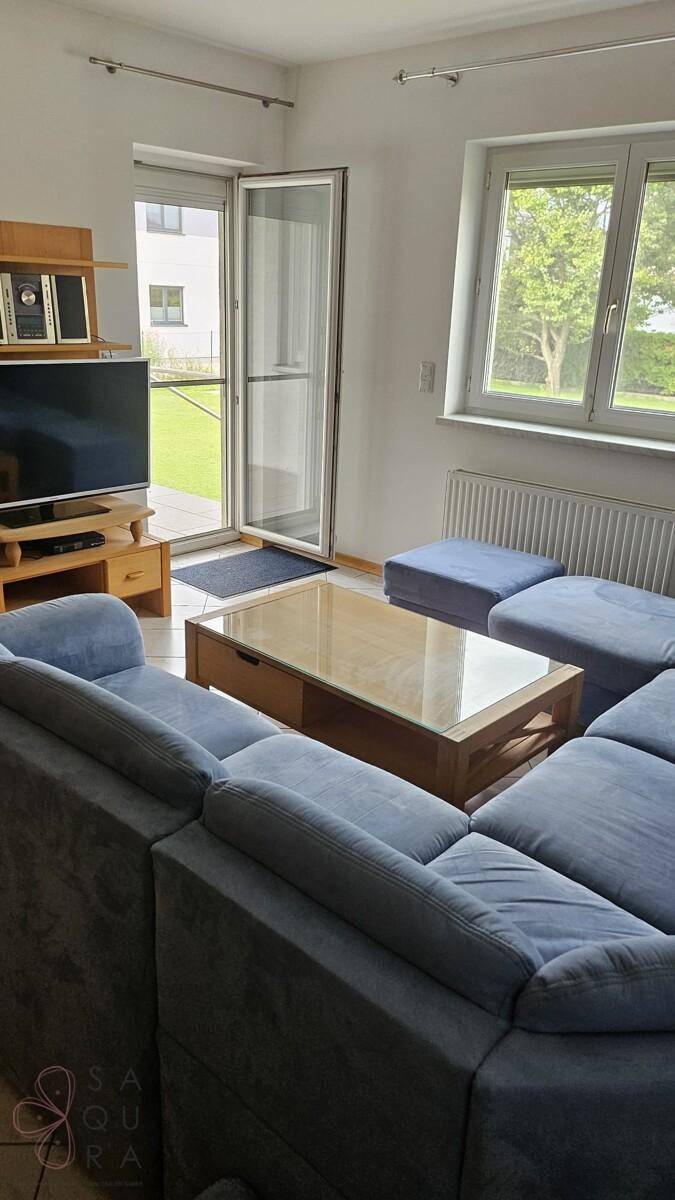 Wohnzimmer mit blauer Eckcouch, Couchtisch und Blick in den grünen Garten.