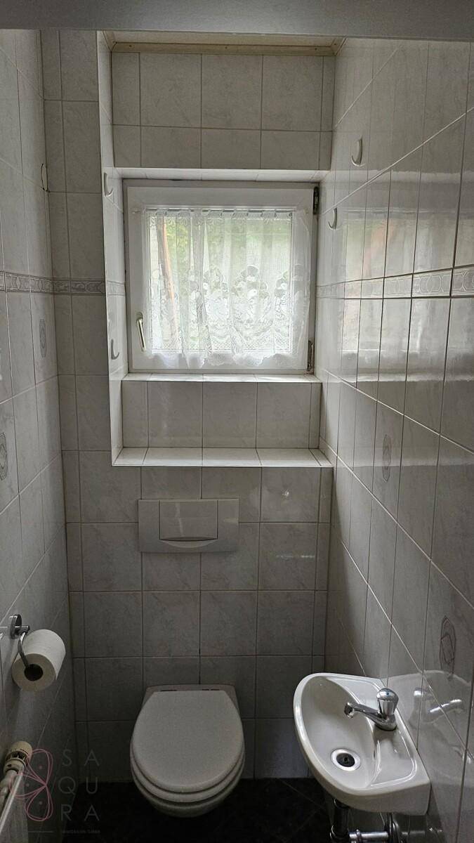 Separate Toilette mit Fenster, Wand-WC und kleinem Waschbecken.