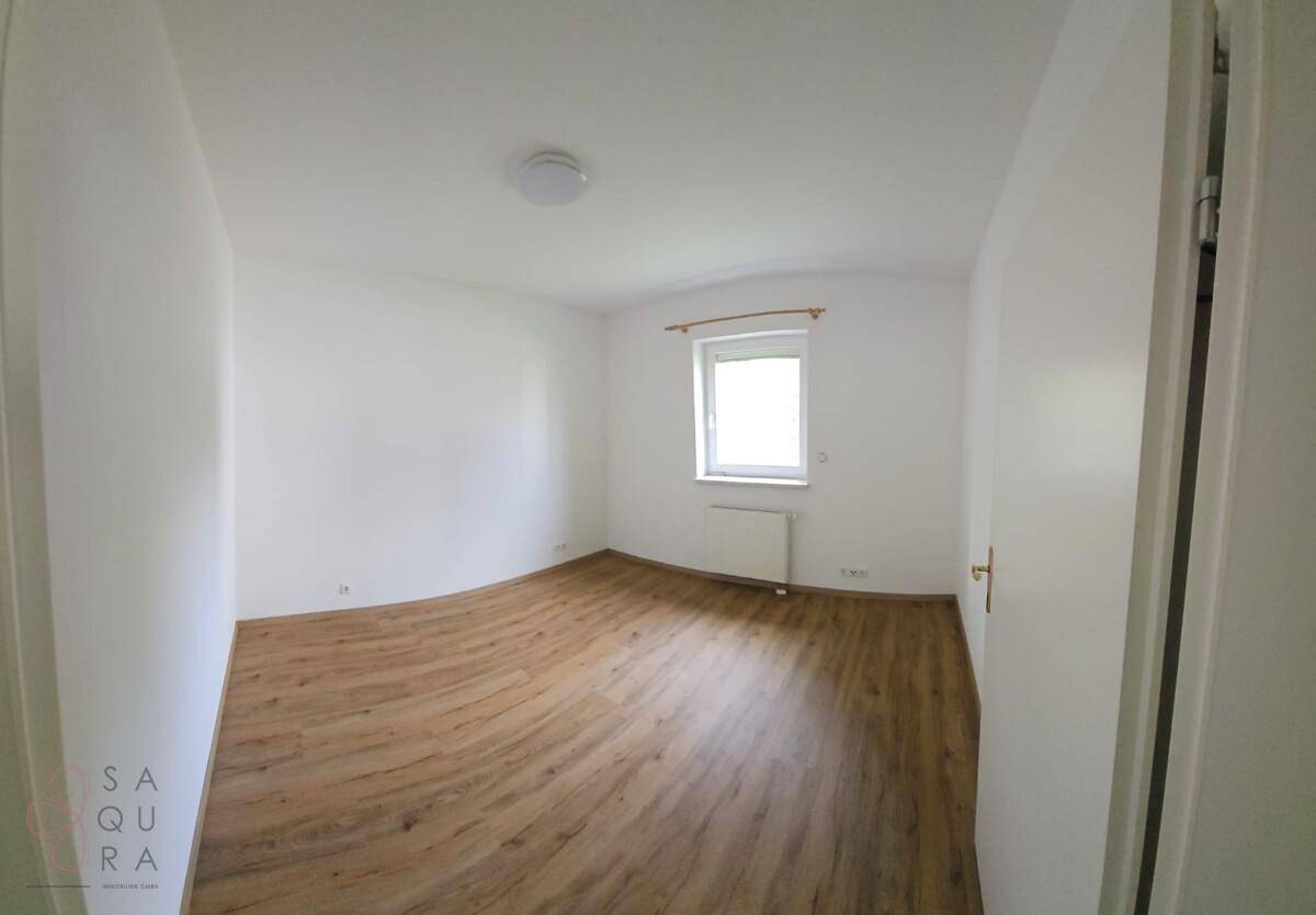 Helles Schlafzimmer mit Laminatboden und einem Fenster, das viel Tageslicht hereinlässt.
