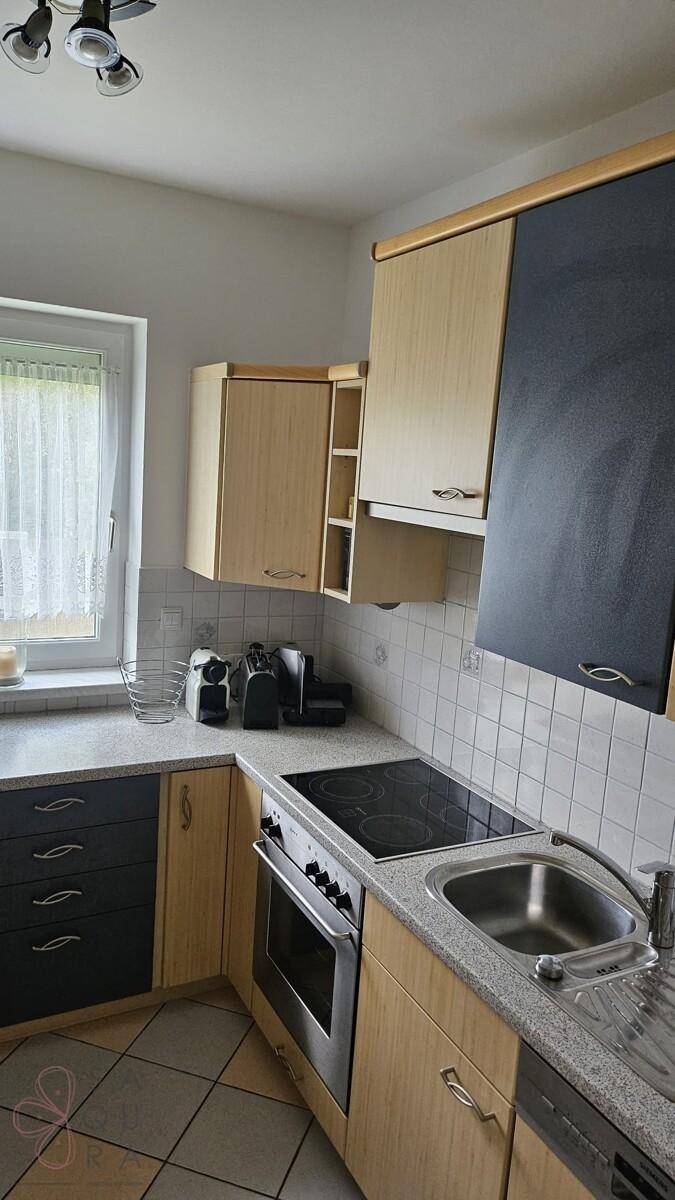 Funktionale Küche mit Induktionskochfeld, Backofen und Spüle, umgeben von Holzschränken.