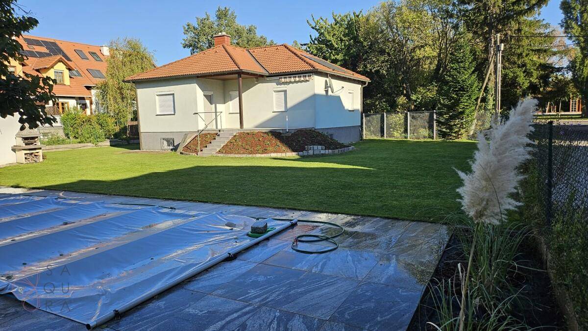 Freistehendes Haus mit großem Garten, abgedecktem Pool und üppiger Vegetation im Sonnenlicht.