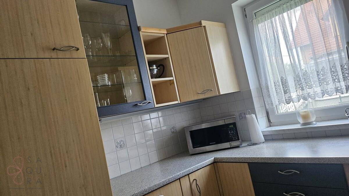 Küche mit hellen Holzfronten, dunklen Akzenten und Mikrowelle über der Arbeitsplatte.