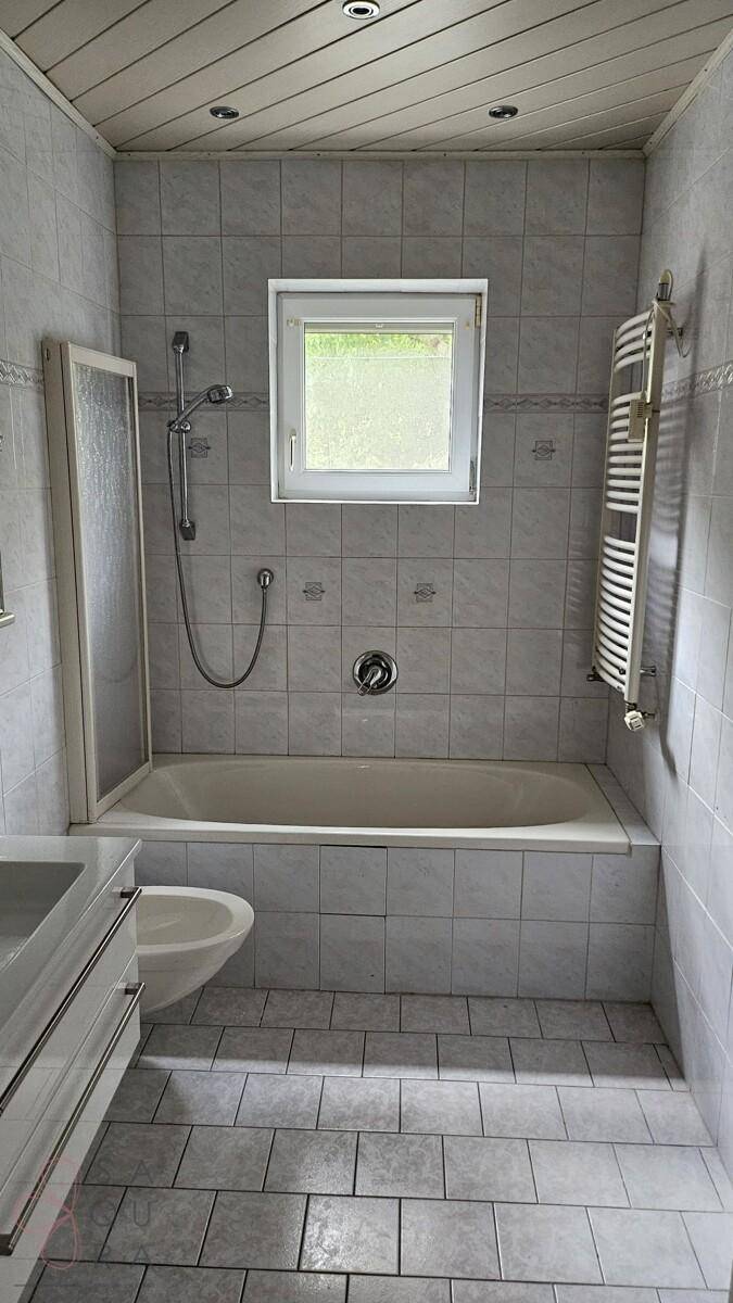 Badezimmer mit Badewanne, Duschvorrichtung, Fliesen und beheiztem Handtuchhalter.