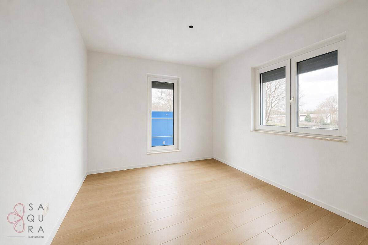 Ein helles, leeres Zimmer mit Laminatboden und zwei Fenstern, bereit zur individuellen Gestaltung.