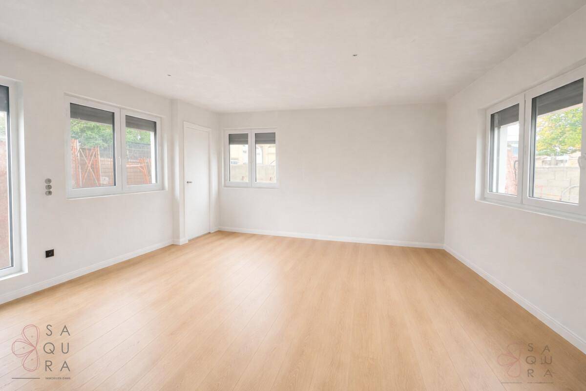 Helles, leeres Wohnzimmer mit Laminatboden und mehreren Fenstern für viel Tageslicht.
