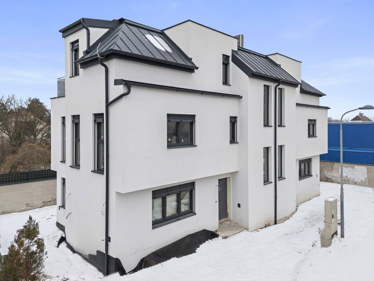 Die moderne Architektur des Neubaus im Winter, umgeben von Schnee und kahlen Bäumen.