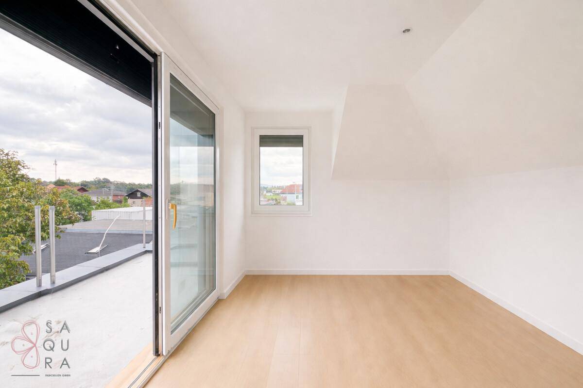 Helles Zimmer mit Dachschräge, Laminatboden und direktem Zugang zu einer Dachterrasse.
