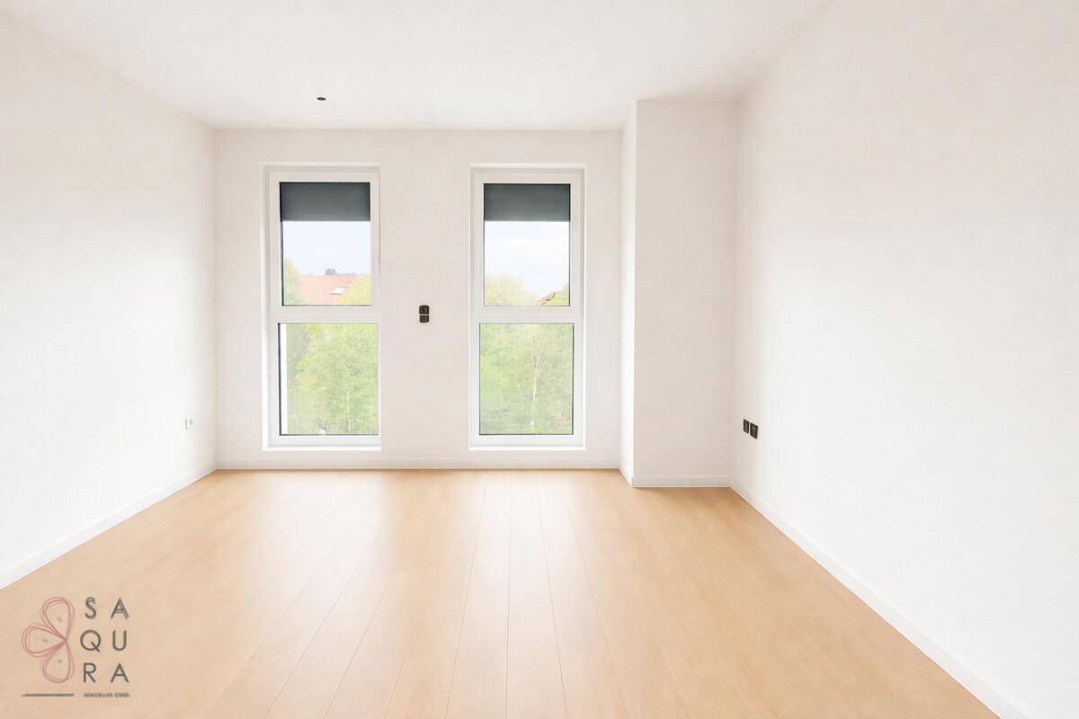 Ein geräumiges, leeres Zimmer mit Laminatboden und großen Fenstern, die viel Licht hereinlassen.