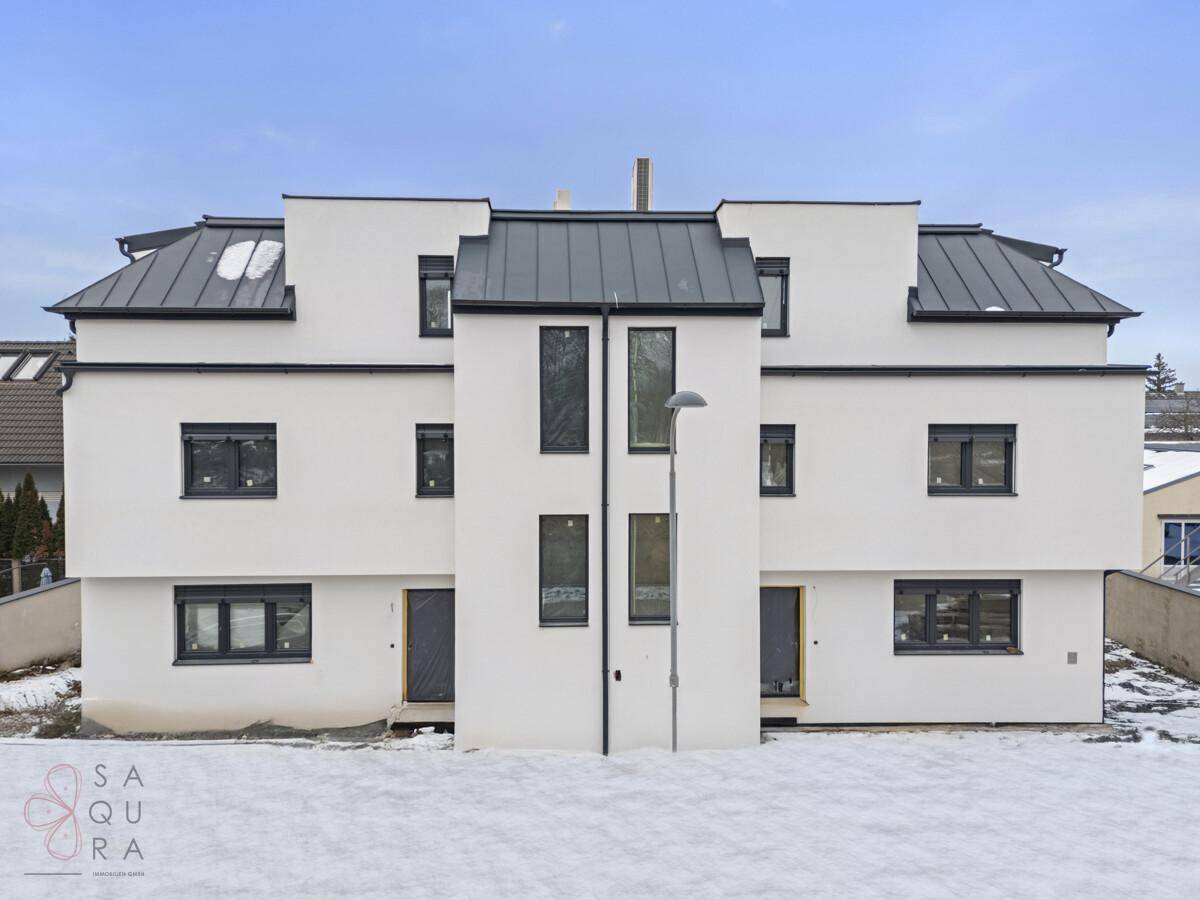 Frontansicht des Neubaus im Winter mit weißer Fassade und dunklen Dächern, umgeben von Schnee.