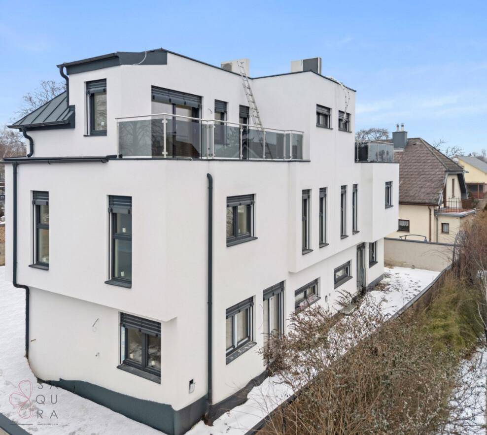 Seitliche Ansicht des Neubaus im Winter mit weißer Fassade, dunklen Fenstern und Terrassen.