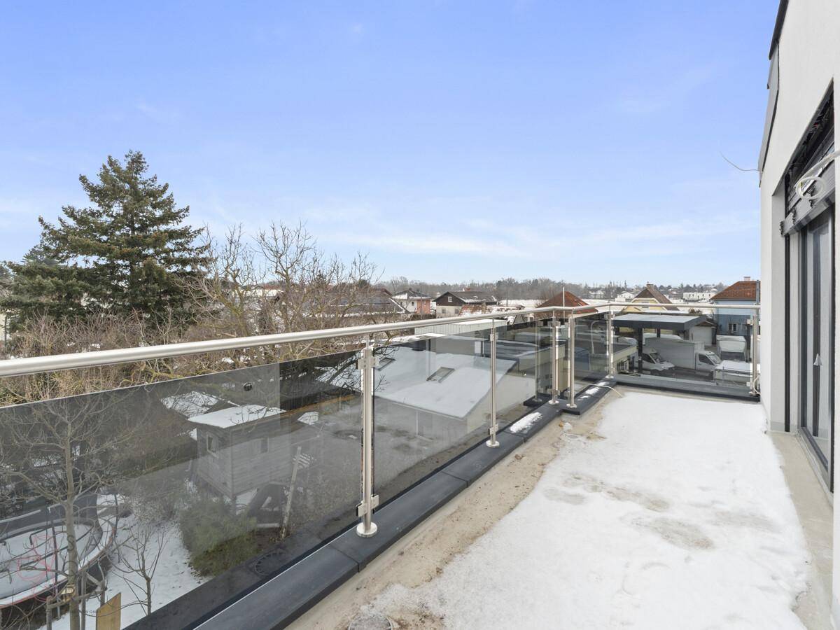 Geräumiger Balkon mit Glasgeländer und Blick auf die umliegende Wohngegend im Winter.