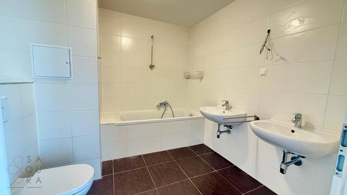 Gefliestes Badezimmer mit Badewanne, Doppelwaschbecken und Toilette.