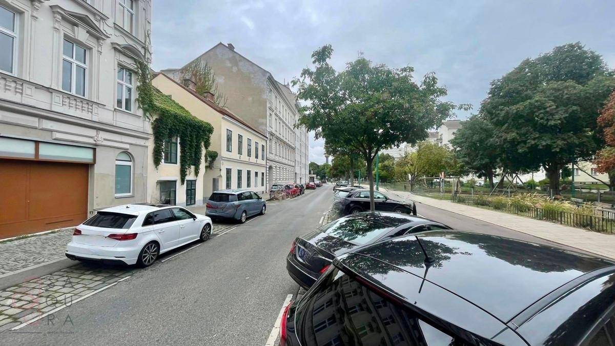 Ruhige Wohnstraße mit parkenden Autos, Bäumen und historischen Gebäuden an einem bewölkten Tag.