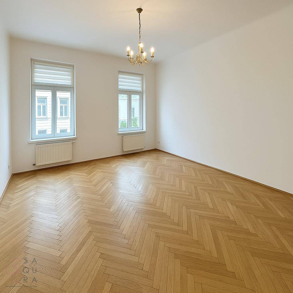 Geräumiges, unmöbliertes Zimmer mit Fischgrätparkett, hohen Decken und großen Fenstern.