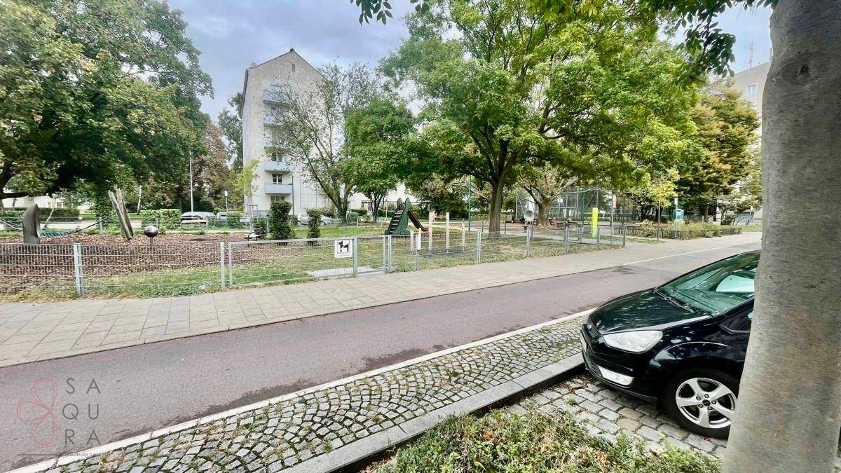 Grüner Stadtpark mit Spielplatz, Bäumen und einem gepflasterten Weg neben der Straße.