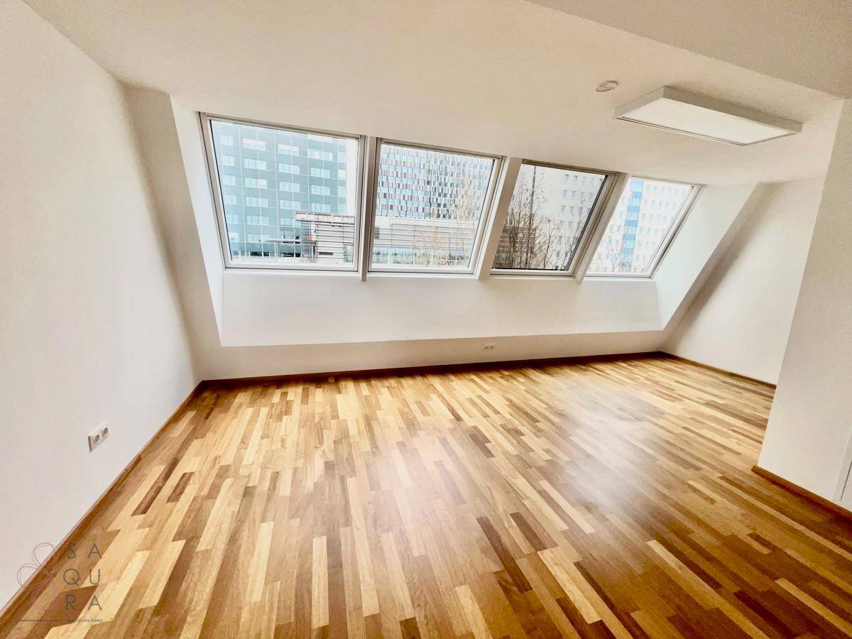 Geräumiges Zimmer mit Holzboden und breiter Dachfensterfront, bietet viel Tageslicht.