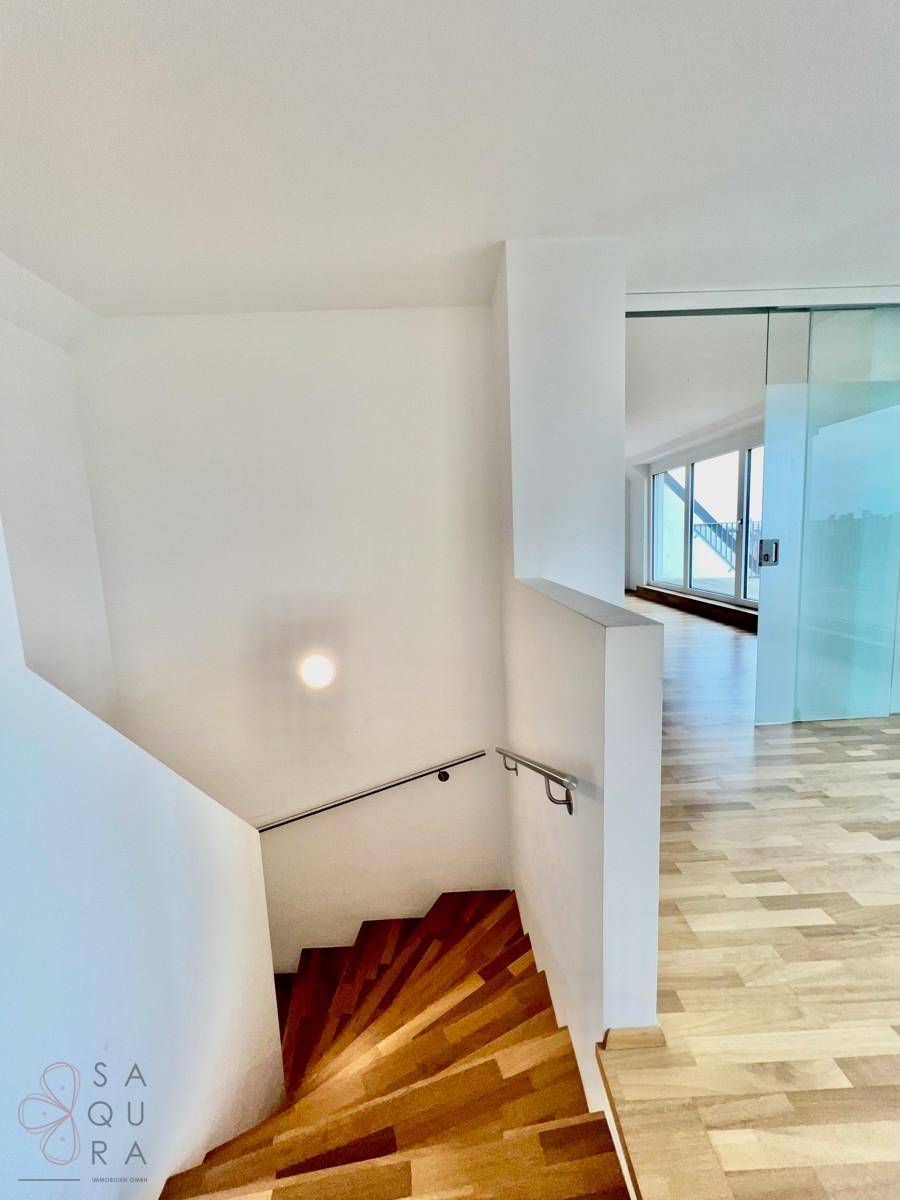 Treppenhaus mit Holzstufen und modernem Geländer, führt in die unteren Wohnbereiche.