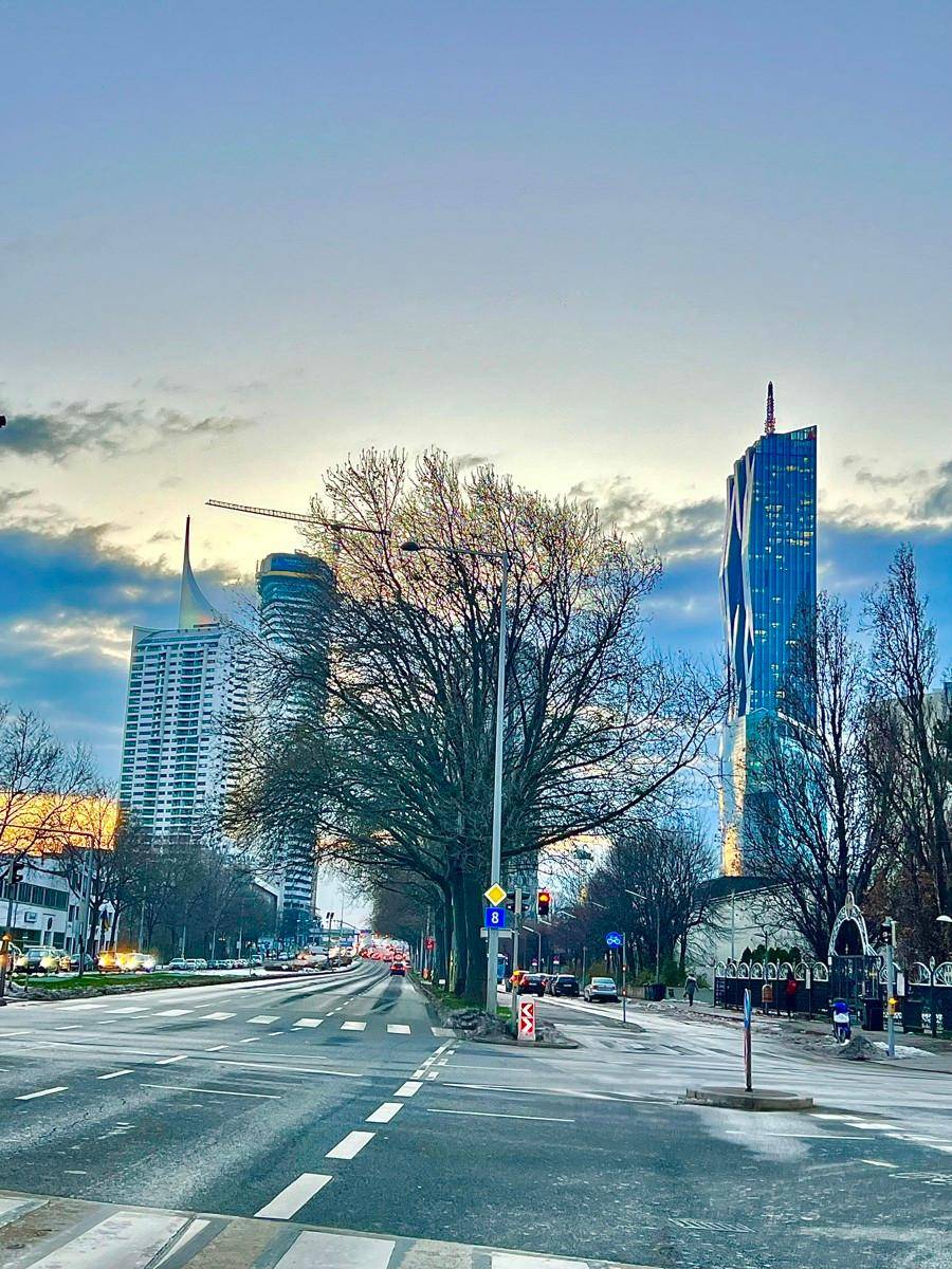 Urbane Szene mit markanten Wolkenkratzern und einer breiten Straße bei Sonnenuntergang.