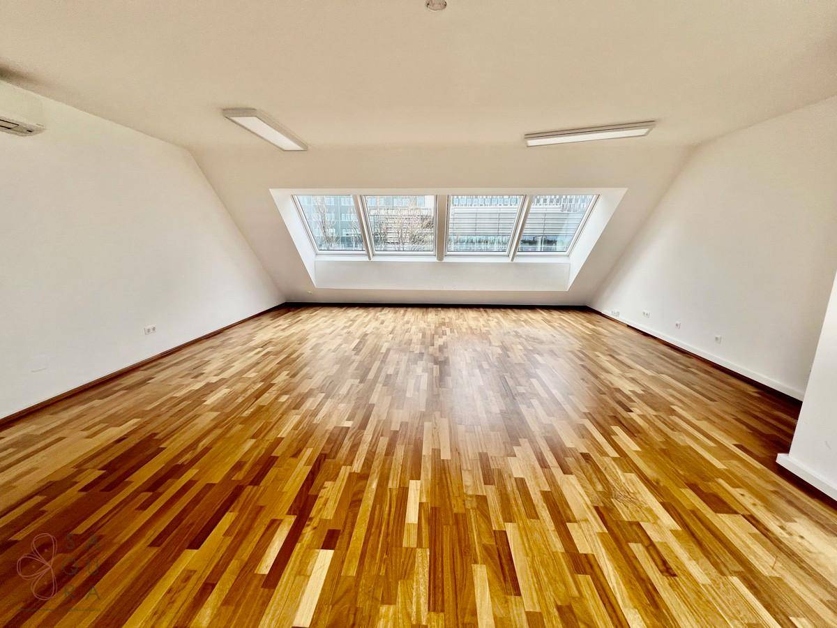 Geräumiges Zimmer mit Holzboden und breiter Dachfensterfront, bietet viel Tageslicht.