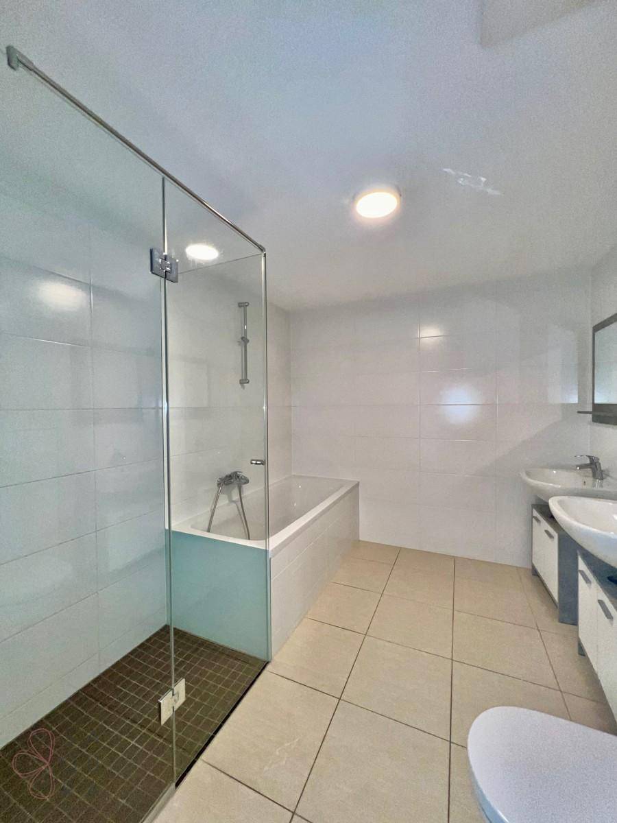 Modernes Badezimmer mit Badewanne, Duschbereich und Doppelwaschbecken in hellen Farbtönen.