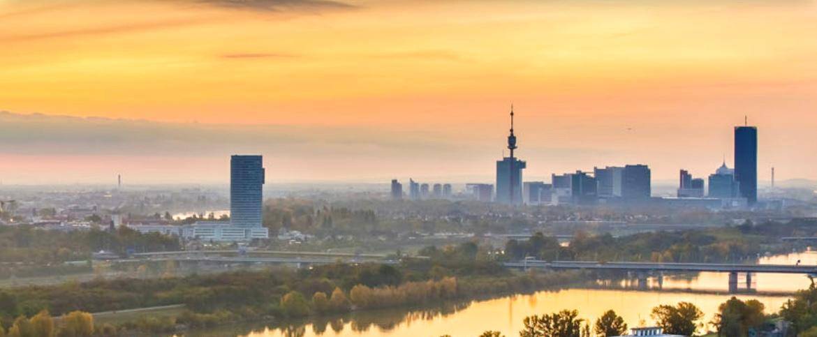 Panoramablick auf eine Stadtlandschaft mit Fluss, Brücken und Hochhäusern bei Sonnenuntergang.