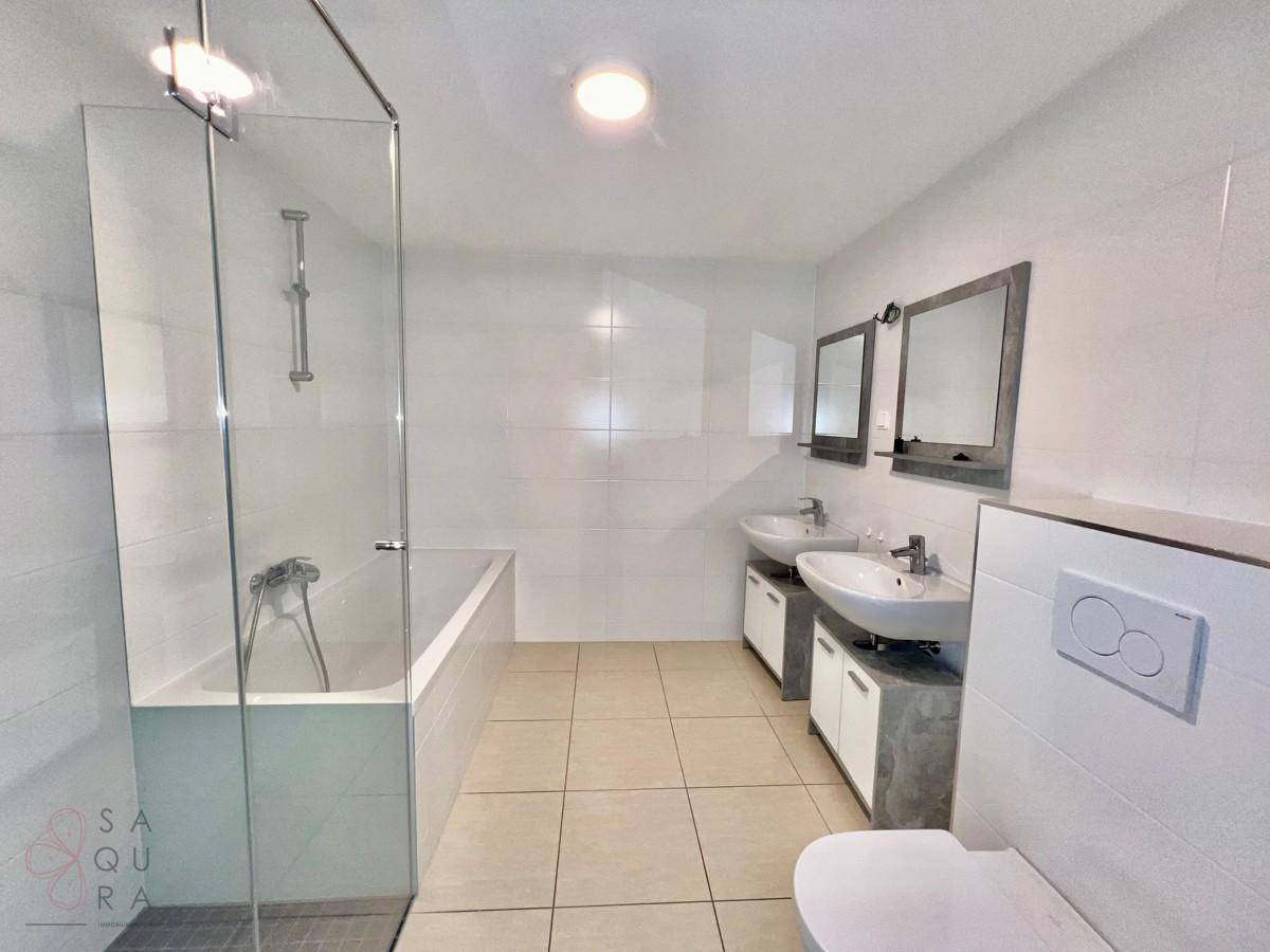 Helles Badezimmer mit weißen Fliesen, Badewanne, Duschbereich und zwei Waschbecken.
